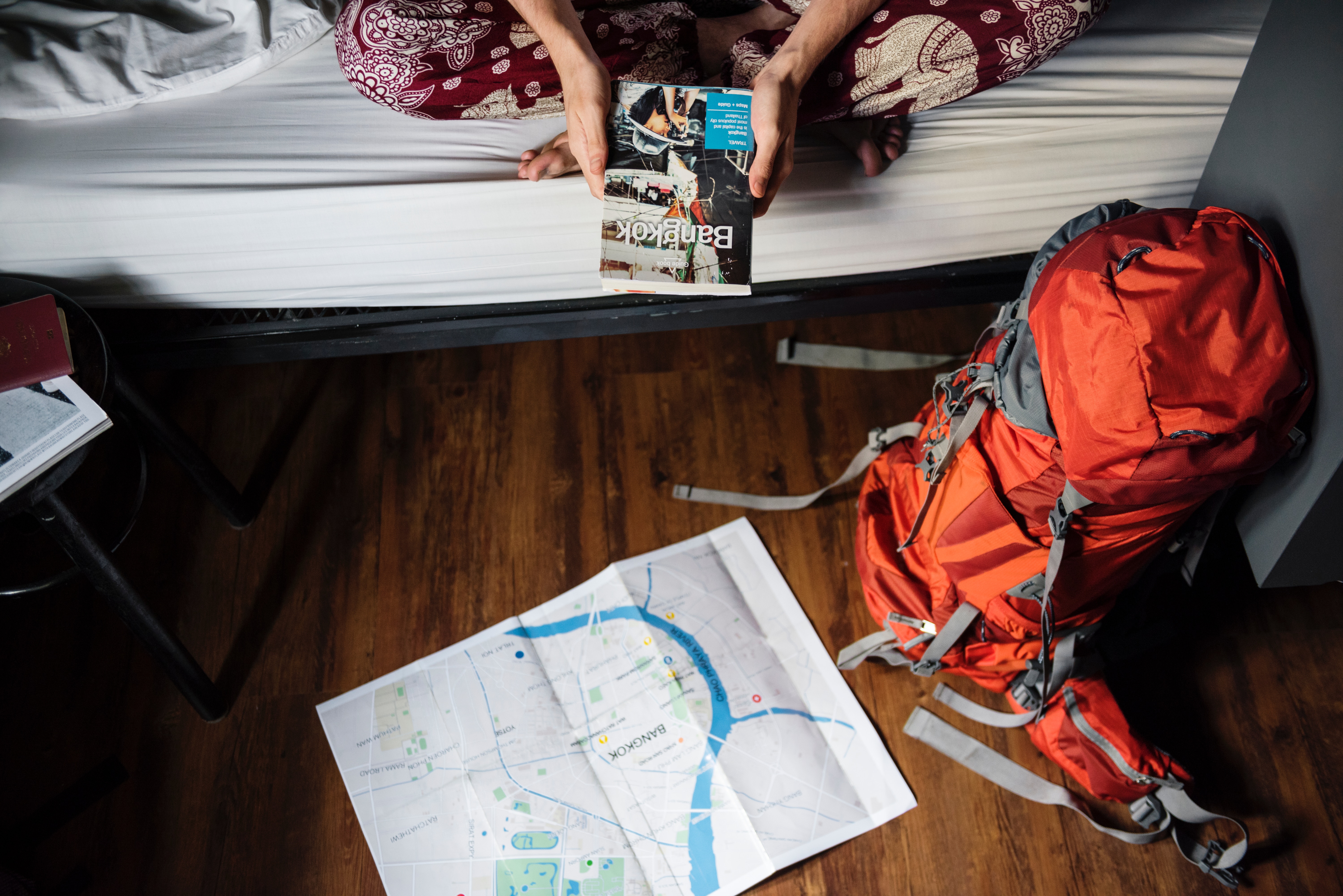 person on bed with lonely planet book and backpack and map