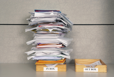 Tall stack of papers in wooden inbox, short stack in wooden outbox