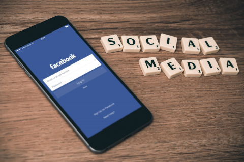 Ignoring social media can be a costly mistake, but easy to fix Facebook on a phone next to social media letters scrabble