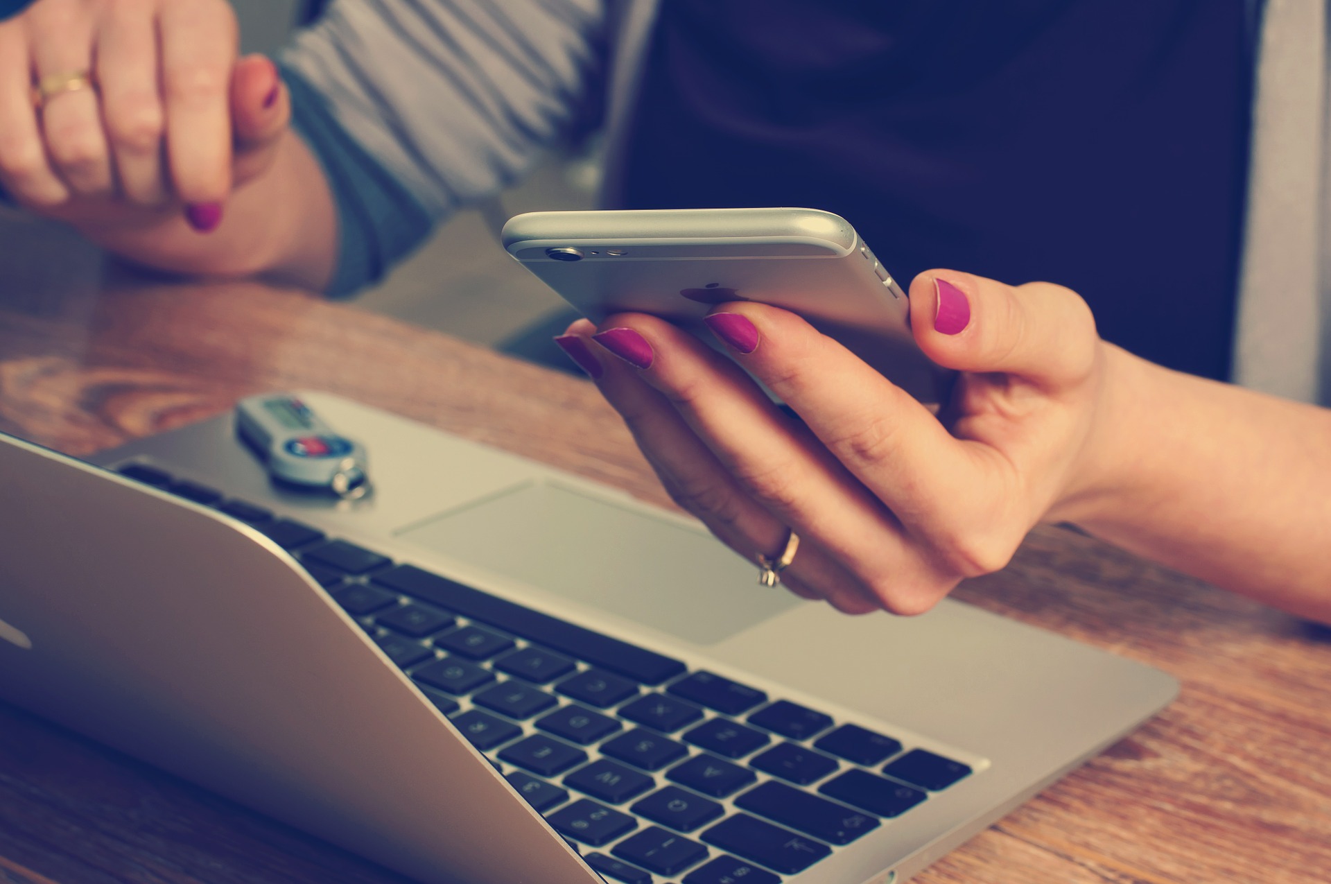 woman holding phone in hand by laptop